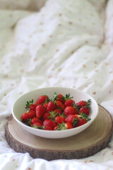 Bowl of fresh strawberries and wooden tray on a bed. Selective focus.