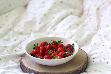 Bowl of fresh strawberries and wooden tray on a bed. Selective focus.