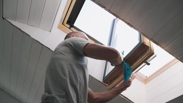 Caucasian man washes the attic window Bright sun illuminates the man in the window during the repair The husband performs finishing work in the house Happy family