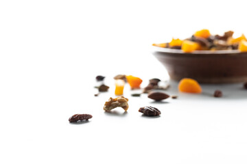 Trail mix scattered on a table with a bowl of trail mix in soft focus in behind against a bright white background.