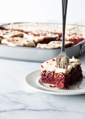 A slice of red velvet chocolate brownie with a fork standing straight up from the slice.