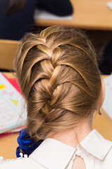 Fototapeta premium Girl's hairstyle braided in a braid fixed with a blue elastic band close-up. Hair styling is done with hairpins and an elastic band. Only the back of the head with a haircut.