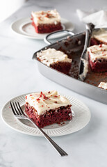 One red velvet brownie on a plate in front, another in behind and a pan of other brownies in the middle.