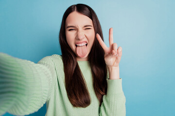 Portrait of rude funky girl hold camera make selfie show tongue hand v-sign on teal background