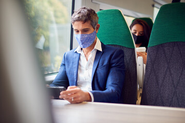 Businessman On Train Streaming To Mobile Phone Wearing PPE Face Mask During Health Pandemic