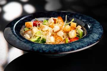 Fresh caesar salad with grilled chicken in a served plate on a black background.