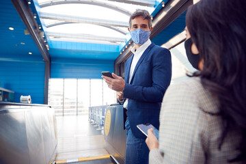 Business Couple Commuting Riding Escalator At Railway Station Wearing PPE Face Masks In Pandemic