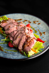 Grilled duck meat with salad on a grey plate on a black background.