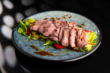 Grilled duck meat with salad on a grey plate on a black background.