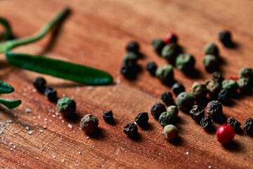 peppercorns are randomly scattered around the table, rosemary lies on the back. on a tree surface. background