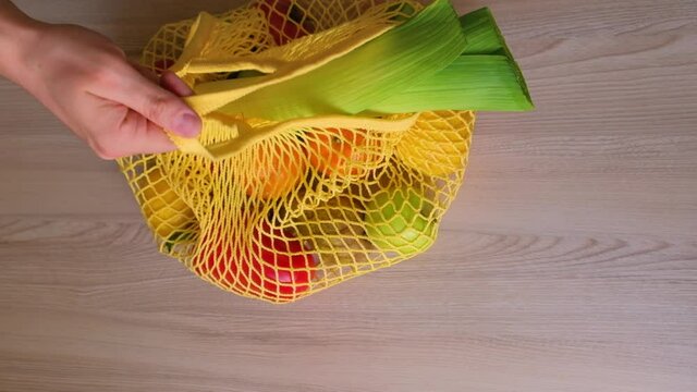 String bag with fresh vegetables and fruits. A somebody puts an eco string bag with fresh vegetables and fruits on the table.
