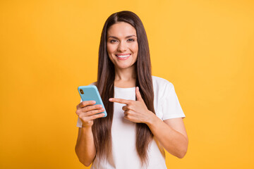 Naklejka premium Photo portrait of woman pointing showing finger at mobile phone advising recommending isolated on vibrant yellow color background