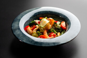Shrimp and vegetable salad in a black plate on a black background. Sea food.
