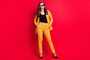Photo of charming funny lady dressed yellow blazer dark glasses smiling arms pockets empty space isolated red color background