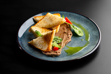 White bread toast, sliced with triangle and pate, decorated with spinach and cherry tomatoes on a gray plate on black.