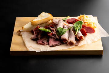 Various meat delicacies in the range. A meat plate. Serving on a wooden cutting dos on a black background.