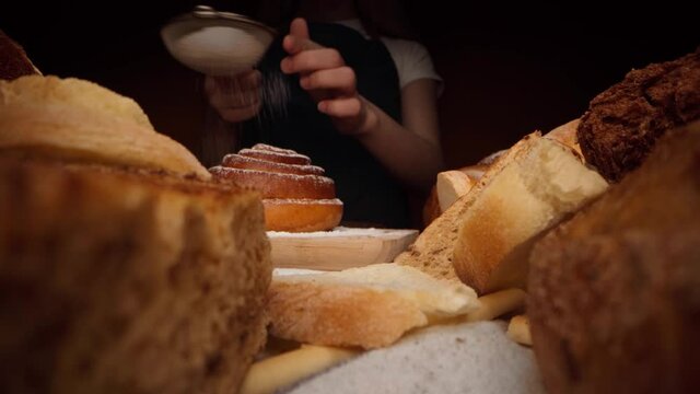 Hands of a baker pouring sugar powder on freshly baked sweet bun