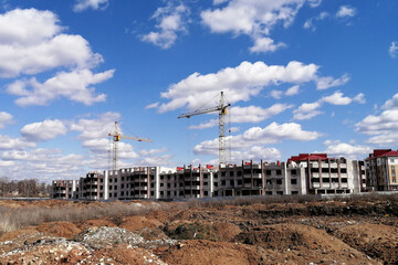 Cranes at construction site against blue sky with clouds