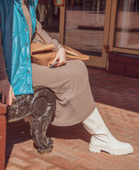 A girl in white leather boots sits on a bench .