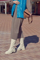 A girl in white leather boots and a knitted dress walks on a sunny day.
