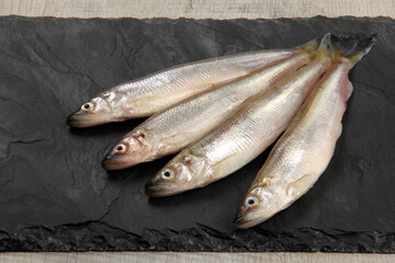Fresh smelt fish on a black stone plate, Smelt fishes (European smelt) with lemon and green parsley, Group of fresh smelt fish 