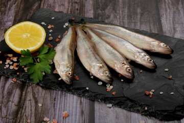 Fresh smelt fish on a black stone plate, Smelt fishes (European smelt) with lemon and green parsley, Group of fresh smelt fish 