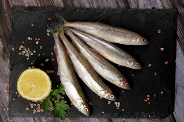 Fresh smelt fish on a black stone plate, Smelt fishes (European smelt) with lemon and green parsley, Group of fresh smelt fish 