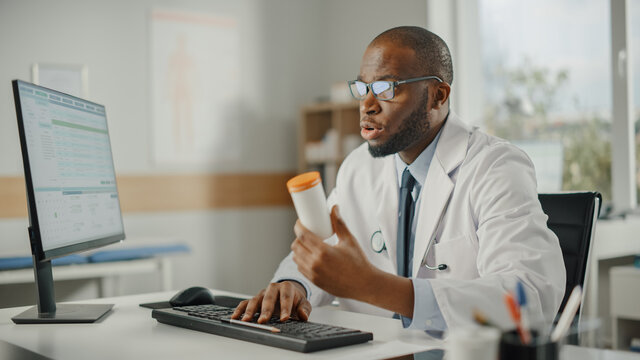 African American Family Doctor is Prescribing Medication to a Patient. Doctor Recommends Pills in a Box to a Patient in a Health Clinic. Physician Sitting Behind a Desk in Hospital Office.
