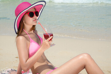 Beautiful Asian girls wearing cute bikini and sunglasses sitting on the beach drinking juice