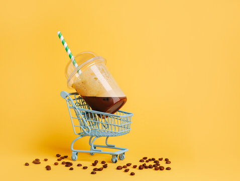 Coffee cup in shopping cart with coffee beans against yellow background. Creative coffee shop delivery or takeaway concept. Delivery service banner with copy space and advertising area.