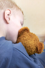 A three-year-old boy kisses his teddy bear, rear view.