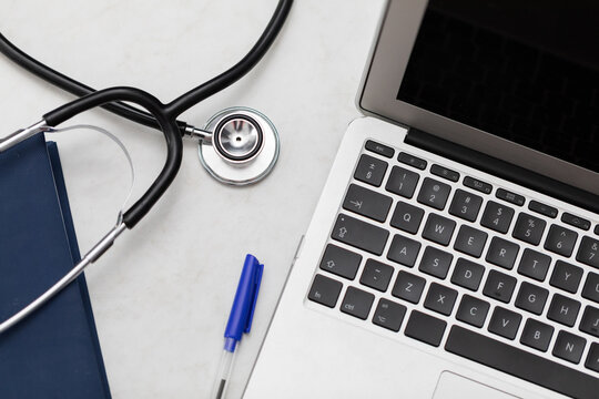 The stethoscope sits on the desk and next to it is a laptop and a book calendar.