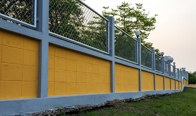Yellow concrete wall fence with steel grating in forest garden.