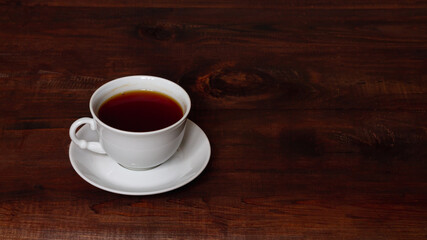 A white cup and saucer on a brown wooden table, breakfast in solitude. copy space