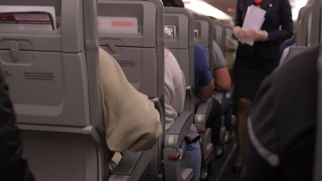Flight plane cabin. Passengers people sitting on seats and flight attendant walking aisle in background at commercial airplane cabin. Travel tourism travelling concept