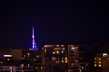 Naklejka premium Tbilisi, Georgia - 17th april, 2021: Tbilisi TV communication tower illuminated at night. View Georgia capital and house buildings at night concept background.