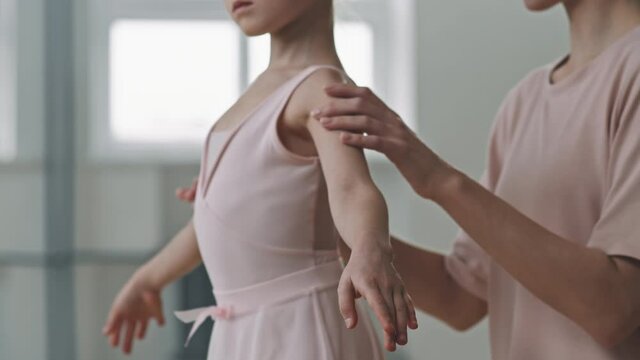 Tilting shot of beautiful little girl learning to stand in ballet poses with help of female trainer practicing in dance school