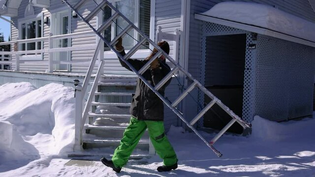 Slow motion shooting of a long haired young man placing an extensible professional ladder on the edge of a roof for a snow removal operation.