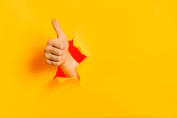 Female child hand gesturing the ok sign, like gesture through torn yellow paper wall, keeps thumb...