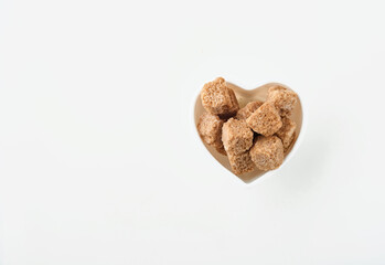 Cane sugar cubes in a white heart shaped bowl isolated on white background.Top view.