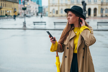 Fototapeta premium Woman using a smartphone and holding a yellow umbrella outside