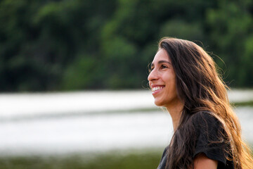 MULHER JOVEM, SORRINDO, LAGOA DESFOCADA NO FUNDO.