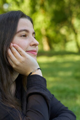 Pretty young woman with long hair in a black shirt and white pants sitting on a blanket of stars on the grass in a park with her bag looking to the sides. teenager resting in nature with blue blanket