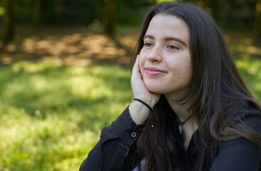 Pretty young woman with long hair in a black shirt and white pants sitting on a blanket of stars on the grass in a park with her bag looking to the sides. teenager resting in nature with blue blanket