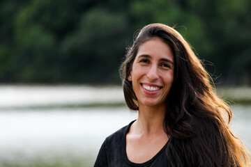 MULHER JOVEM, SORRINDO, LAGOA DESFOCADA NO FUNDO.
