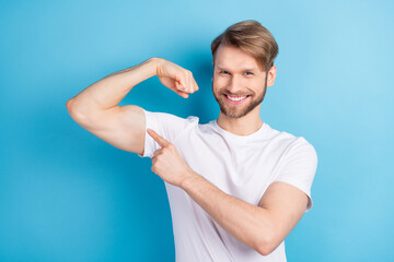 Photo of positive guy indicate finger hand demonstrate biceps look camera isolated on blue color background