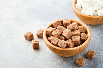 Cane sugar and white sugar cube in bamboo bowl on gray table concrete background. Selective focus.