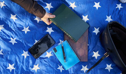 woman's hand with black shirt holding a green book with more blue and brown books with pen and mobile on blue blanket with white stars