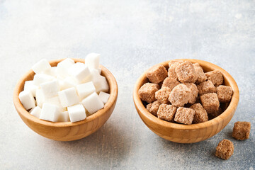 Cane sugar and white sugar cube in bamboo bowl on gray table concrete background. Selective focus.