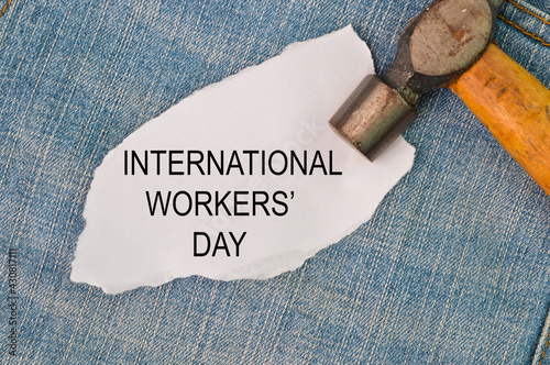 Phrase INTERNATIONAL WORKERS'S DAY written on white paper with hammer and blue jeans.